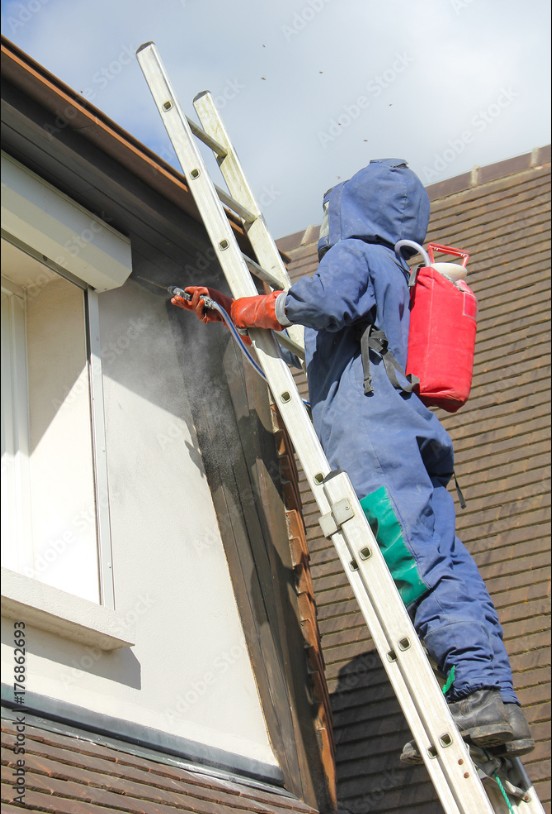 Technicien en dératisation utilisant un spray sur le mur d'un bâtiment, monté sur une échelle.